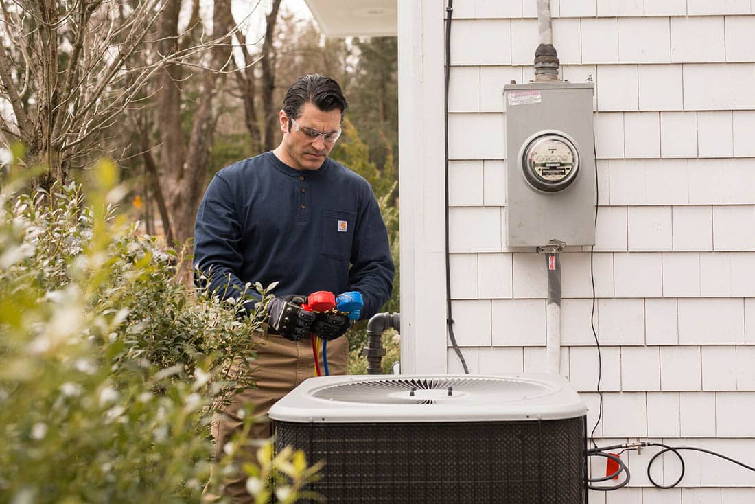 cooling-AirConditioningRepair-Supporting-1100×734 Technician performing air conditioner repair on an outdoor unit on side of house