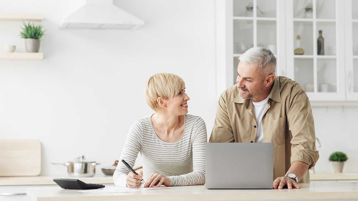 Local HVAC Rebates in Pennsylvania: What Homeowners Should Know 4 Two adults at a kitchen counter review paperwork and a laptop together, with a tablet, pen, and kitchen items visible in a bright, modern space.